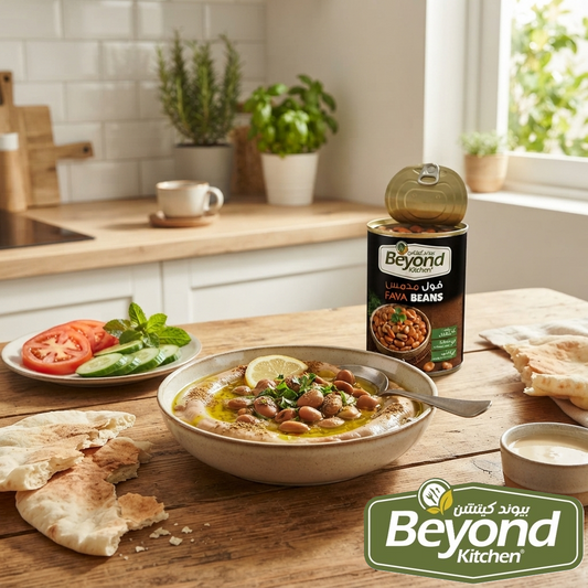 A bowl of Beyond Organic Aromatic Chickpea Hummus on a wooden table, with a can of Beyond Organic Aromatic Chickpea Beans standing behind it. The scene is set in a bright, modern kitchen with a plate of sliced tomatoes, cucumbers, and mint, alongside pita bread and a small bowl of dressing.